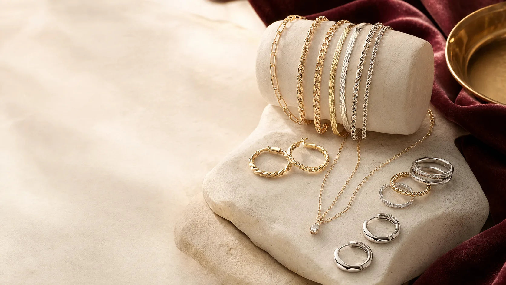 Gold and silver jewelry arranged on ivory stone with burgundy velvet
